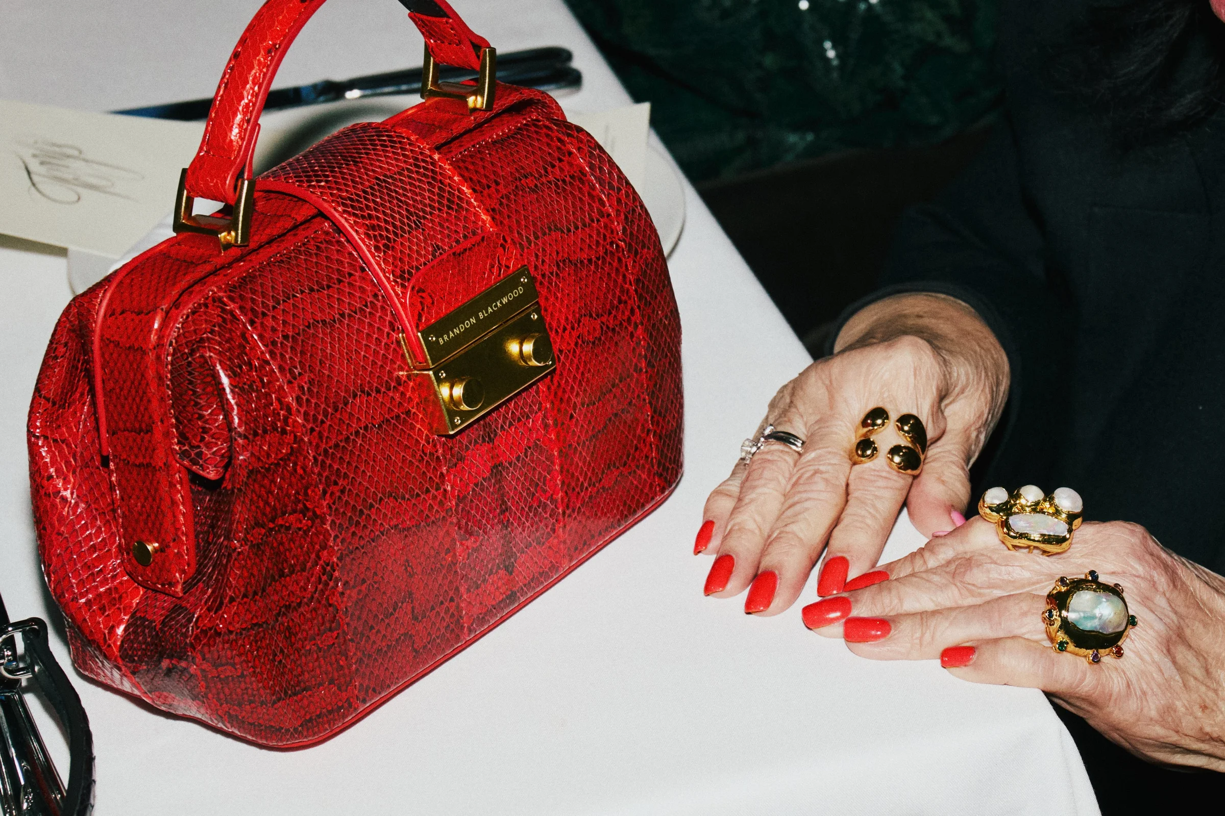 Elizabeth Doctor Bag in red snakeskin on a white tablecloth, a hand with red nails beside it